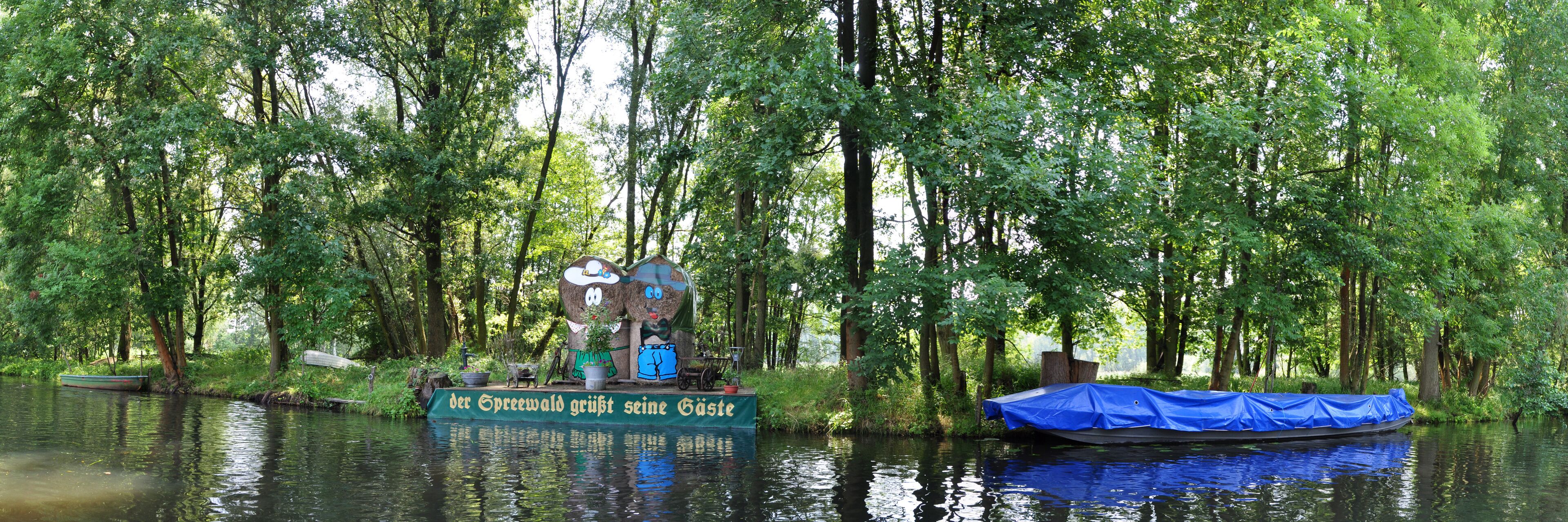 A river with a boat covered in blue tarp and a sign in German.