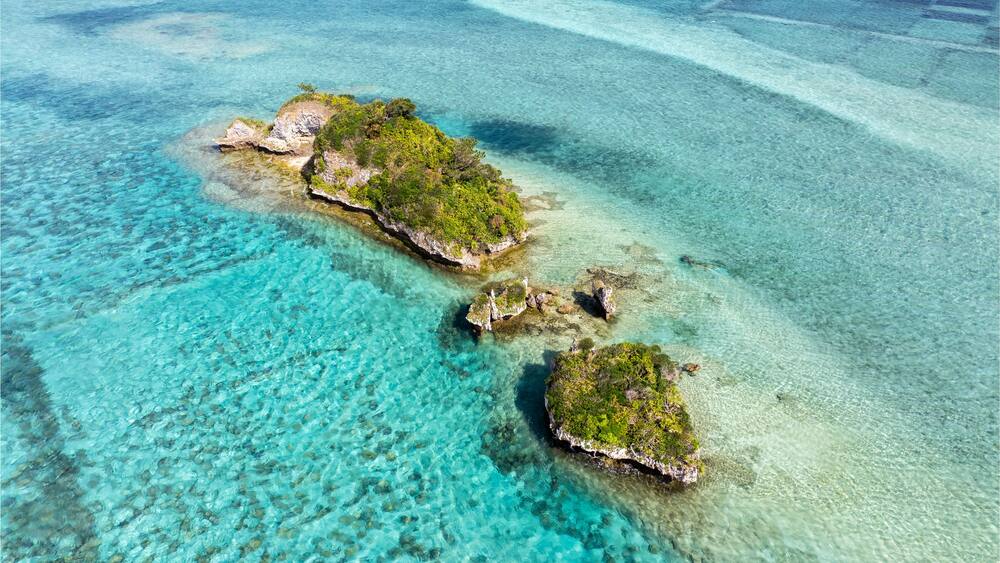 An aerial view of a clear turquoise sea with three small islands covered in green vegetation.