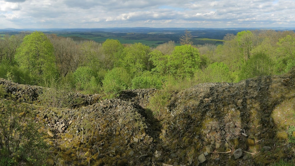 Un paysage rocheux, parsemé de pierres recouvertes de mousse, avec une vallée boisée en arrière-plan.