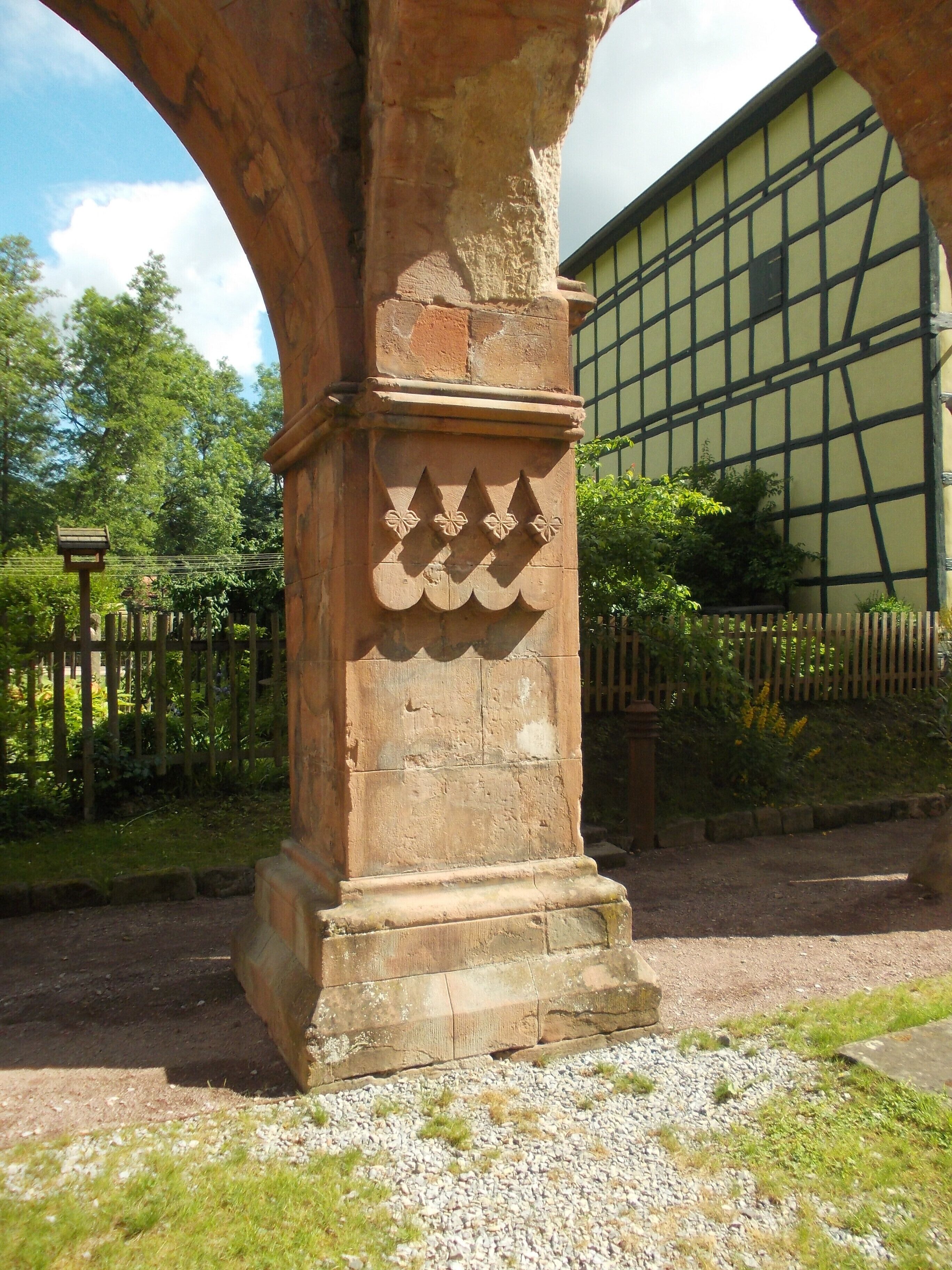 A stone column with carved floral patterns, an archway, and a building with a timber frame facade.