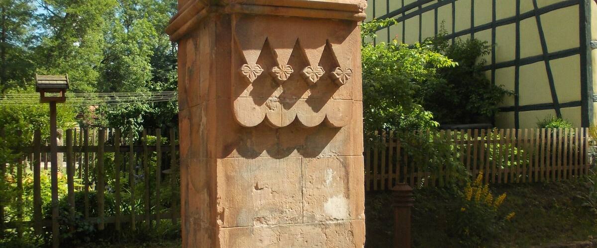 A stone column with carved floral patterns, an archway, and a building with a timber frame facade.