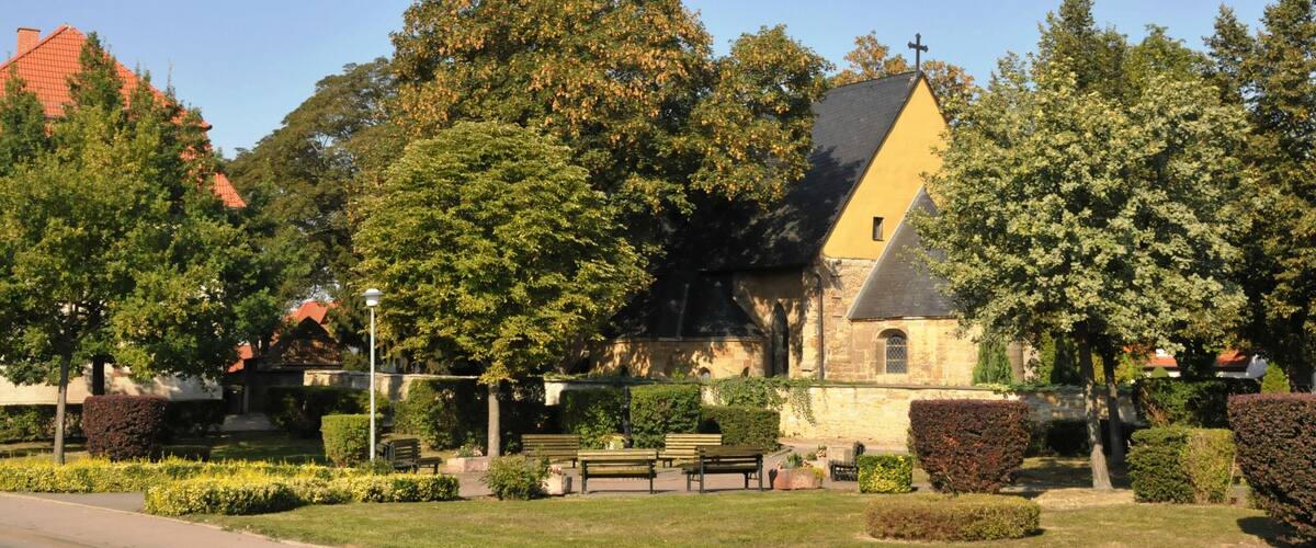 A church with a tall steeple, surrounded by trees and benches in a park.