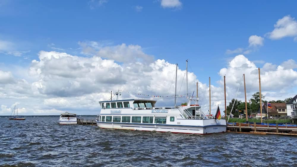 A white boat named 'Steinhude' docked at a pier with a clear sky and clouds.