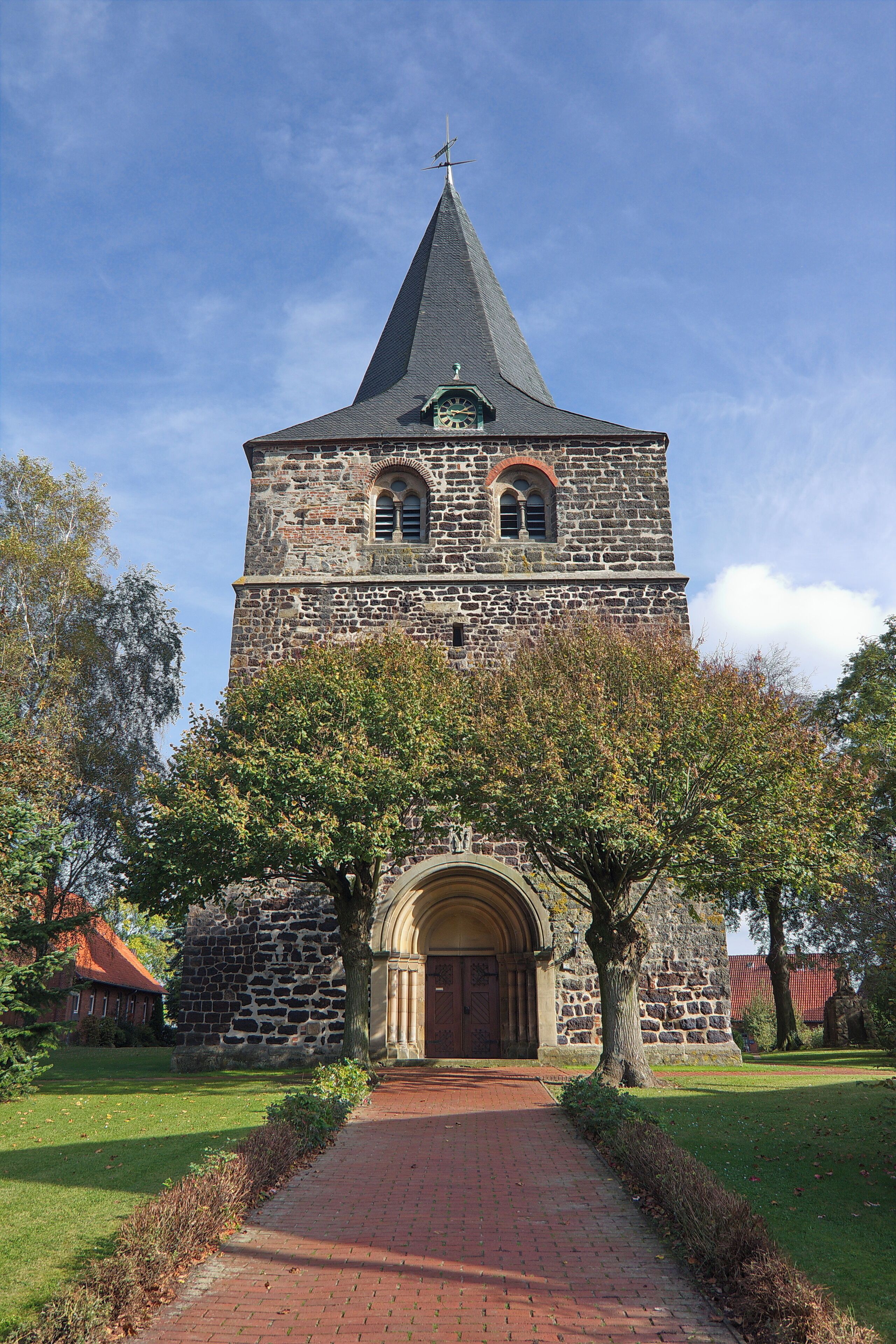 A stone church with a pointed steeple and a brick pathway leading to its entrance.