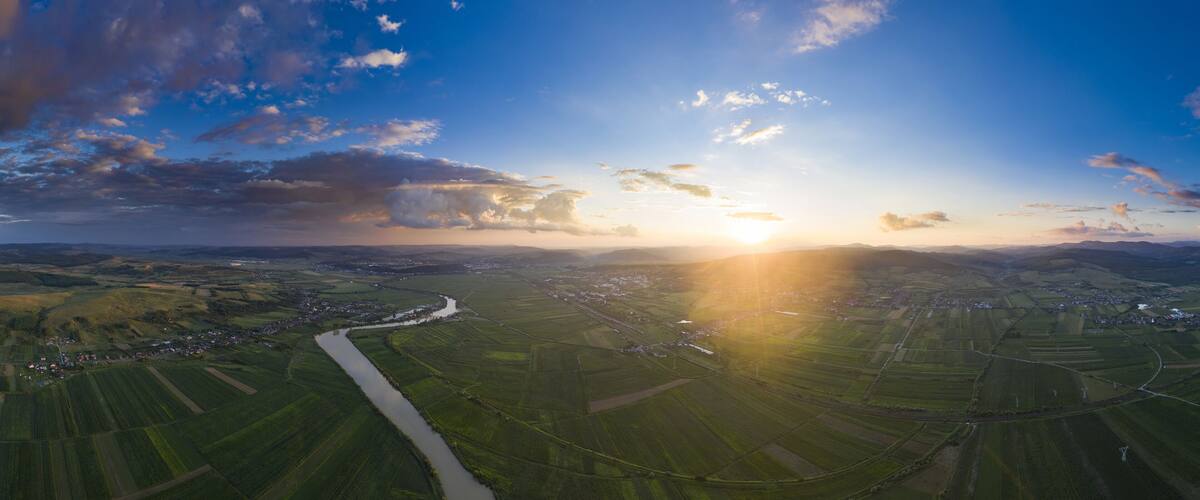 A river winding through green fields, a town in the valley, and a sunset over rolling hills.