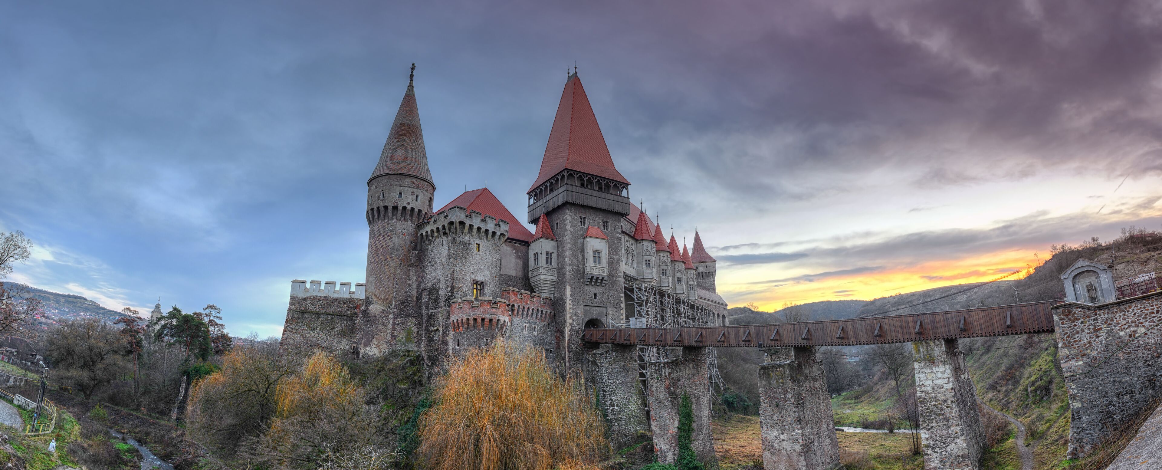 A historic castle with two prominent towers, a bridge, and a river in the foreground.