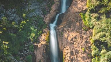 A waterfall cascading down a rocky cliff surrounded by lush greenery.