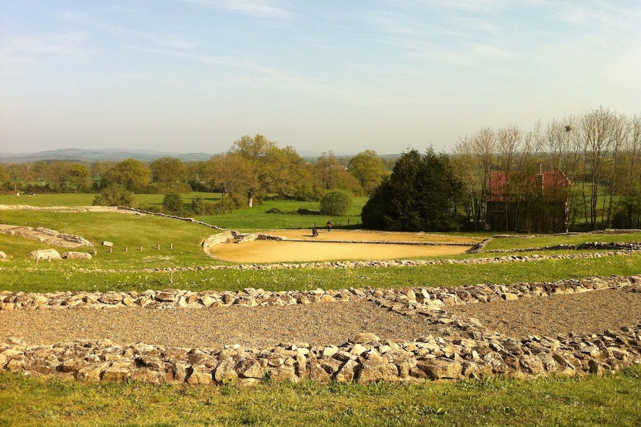 Un site historique doté de murs en pierre et d’une enceinte circulaire, entouré de champs verdoyants et d’arbres.