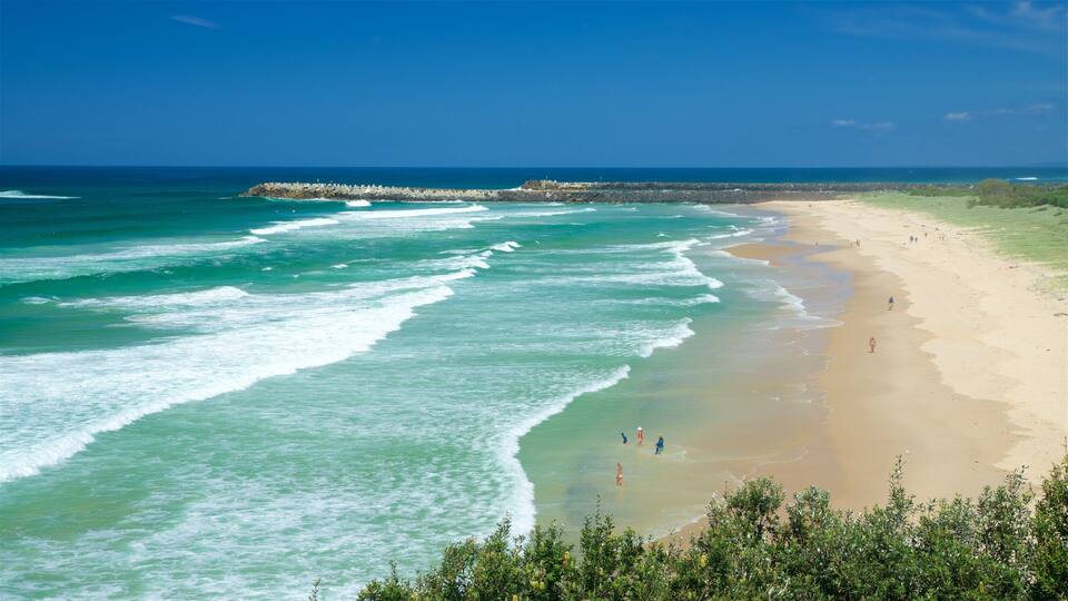 A beach with waves, a rocky breakwater, and people walking along the shore.