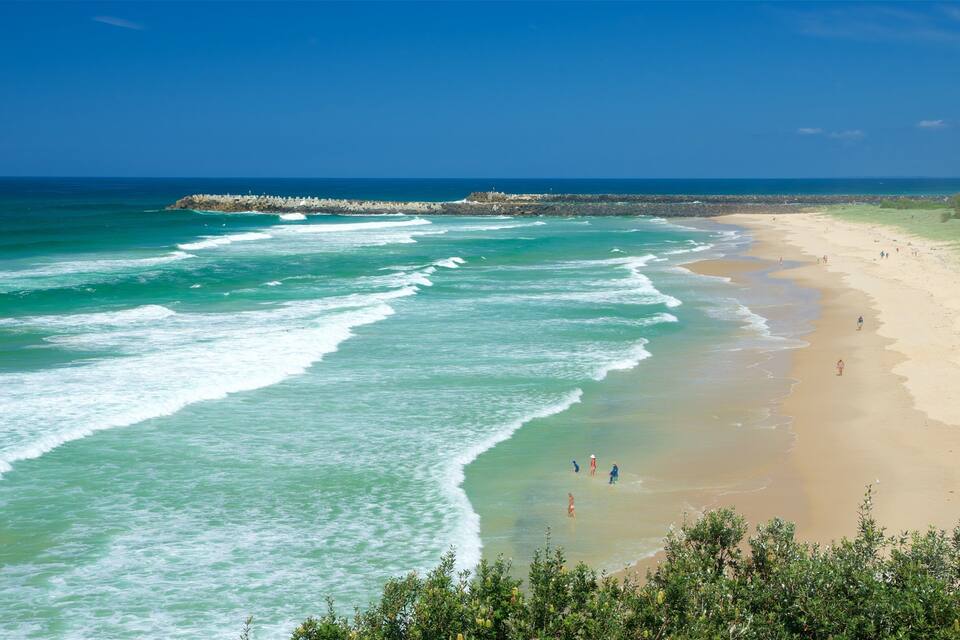 A beach with waves, a rocky breakwater, and people walking along the shore.