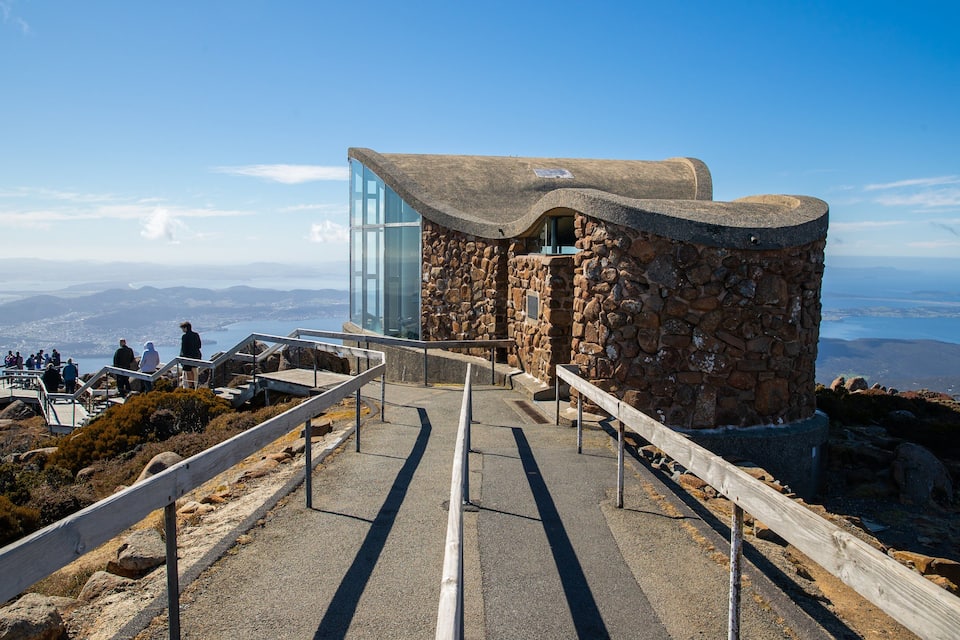 Un edificio de piedra con una plataforma de cristal que ofrece vistas de un paisaje costero.