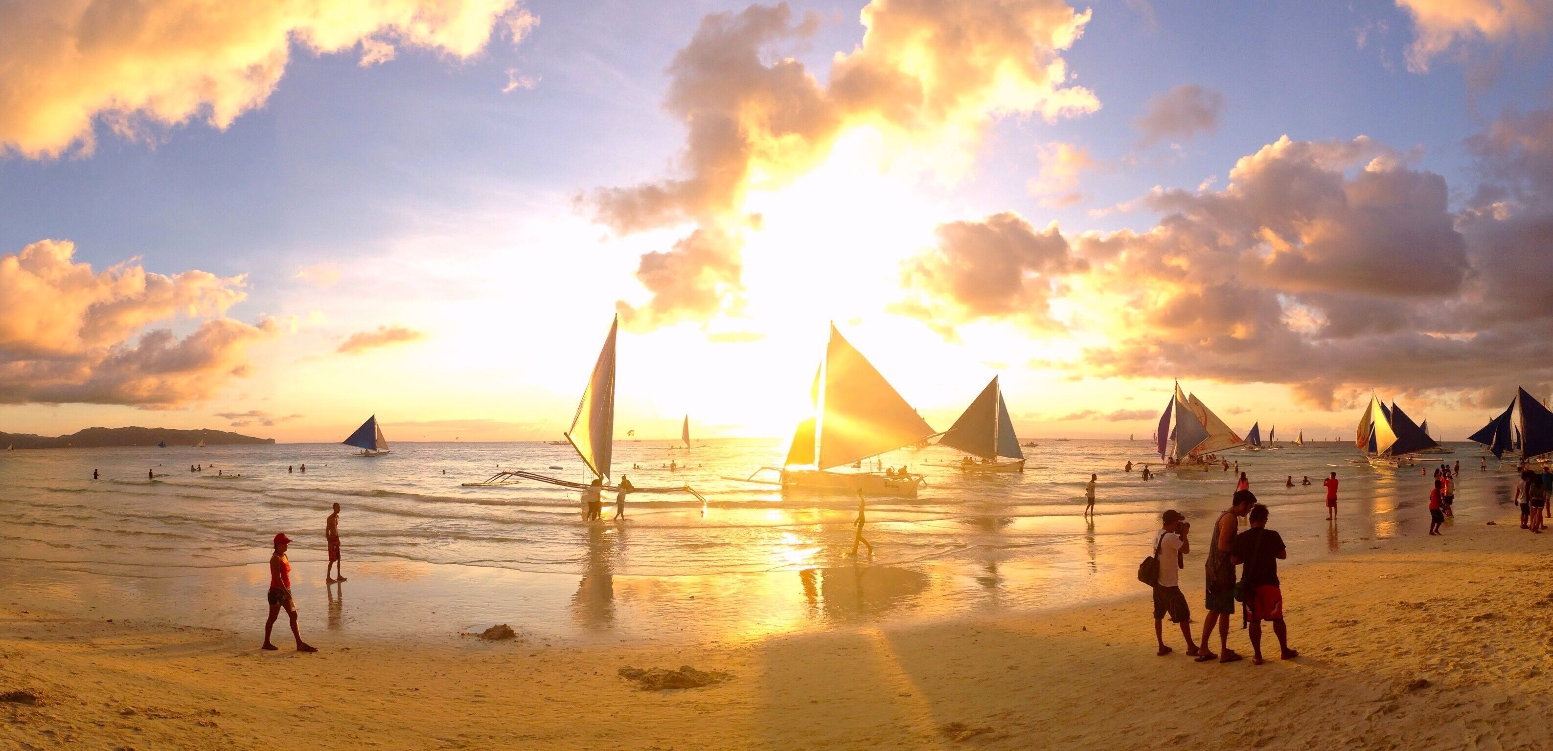 A beach with sailboats and people during sunset.
