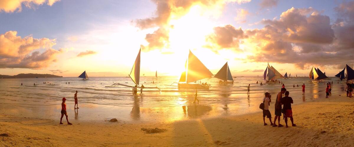 A beach with sailboats and people during sunset.