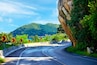 A winding road with sharp bends, surrounded by lush greenery and a mountainous backdrop.