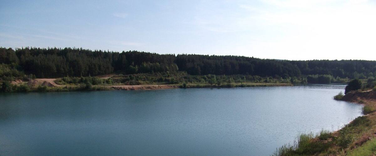A calm lake surrounded by dense forest and a dirt path along the shore.