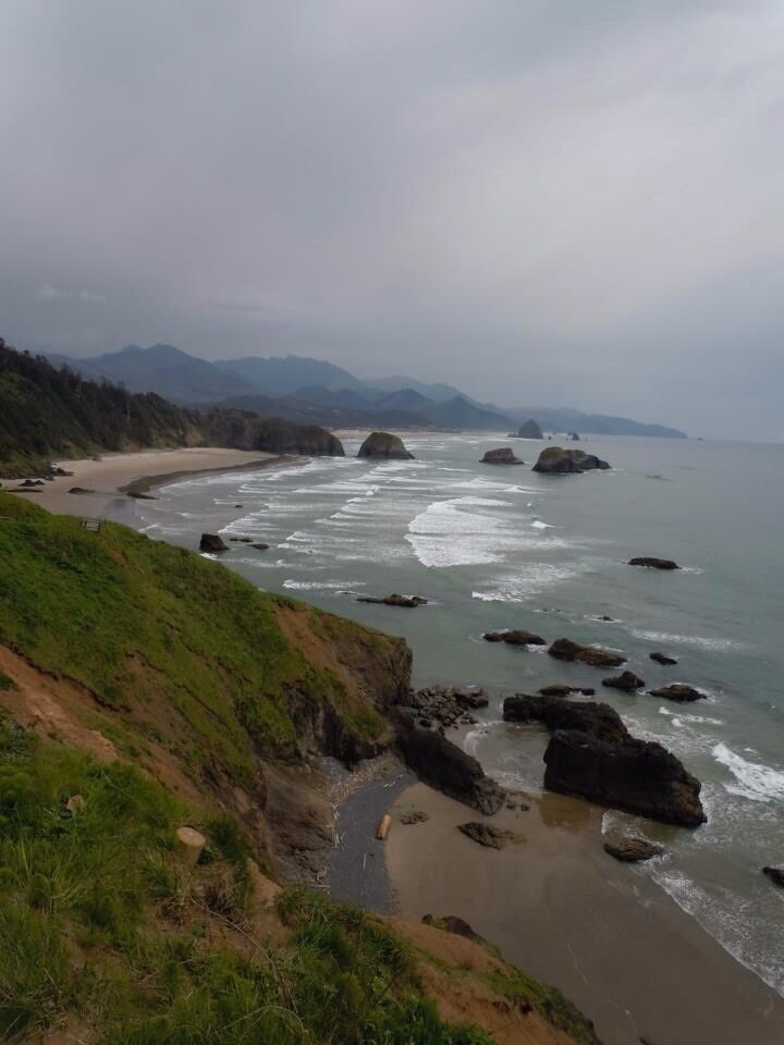 A coastal landscape with a sandy beach, rocky outcrops, and a hilly backdrop.