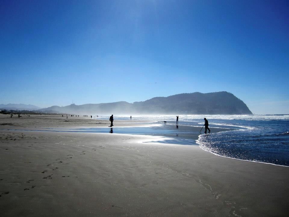 A beach with people walking along the shore, a clear sky, and distant mountains.