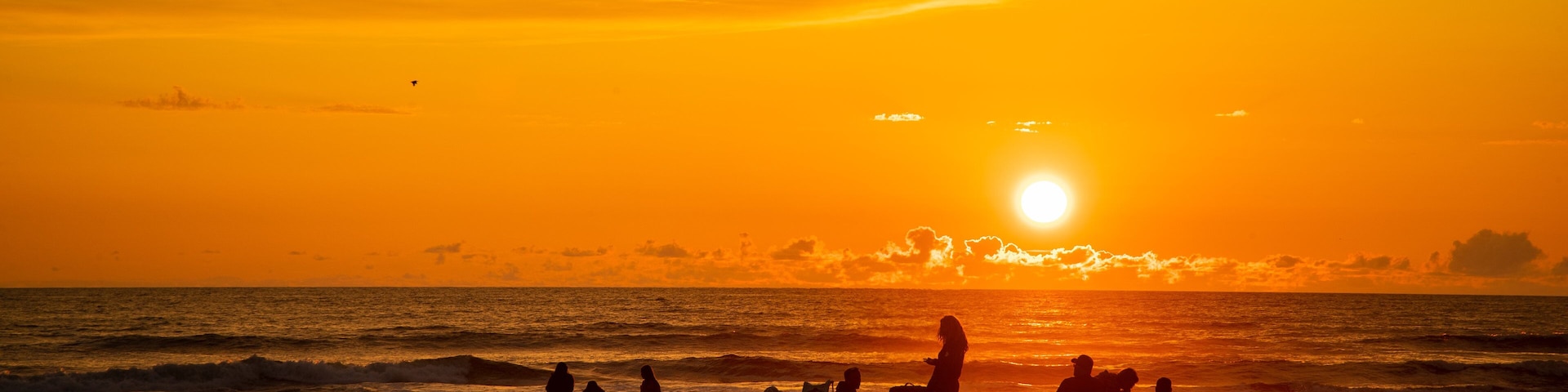 A sunset over the ocean with silhouettes of people on the beach.