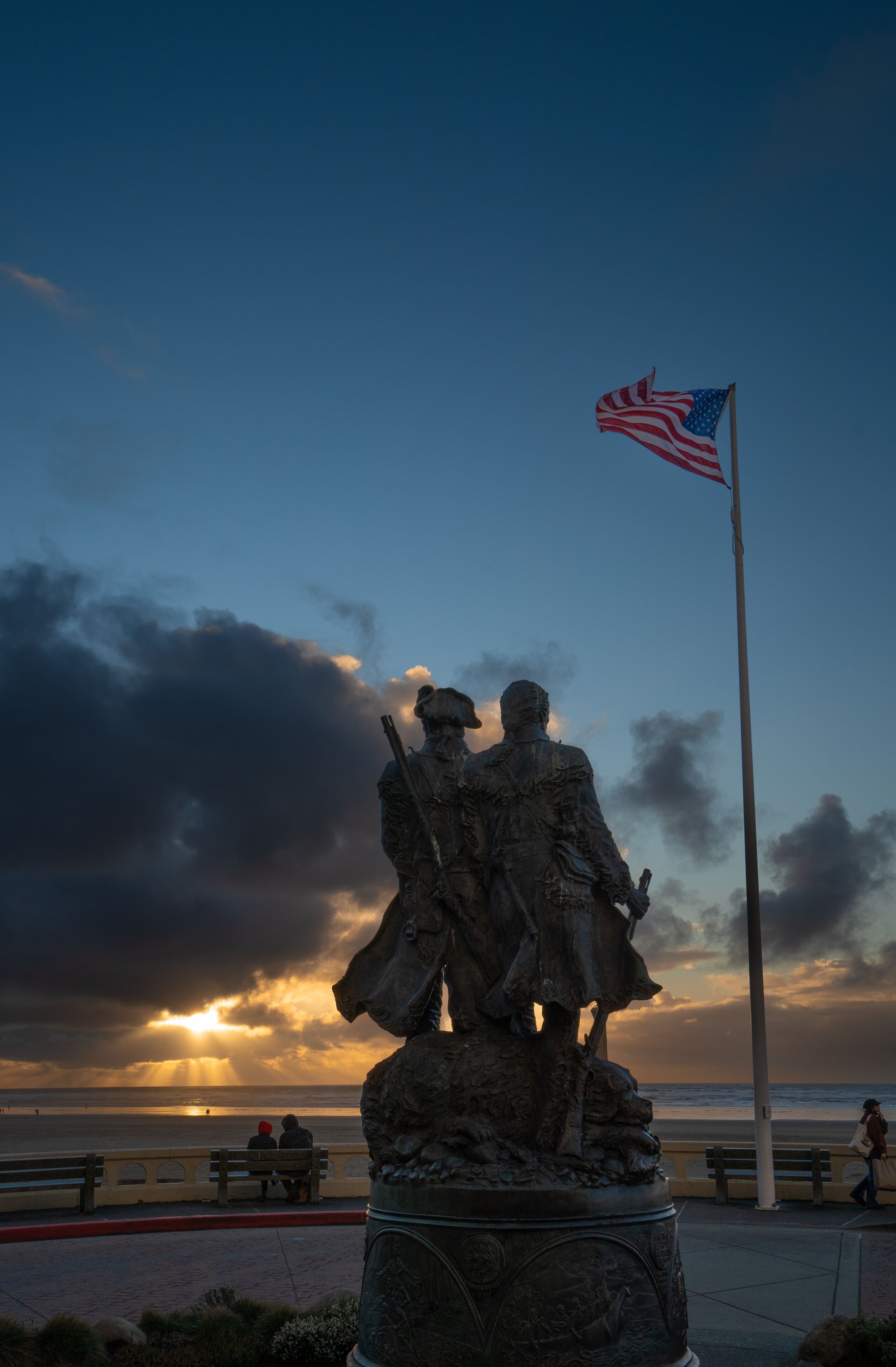 A silhouette of the Lewis and Clark statue at the turnaround at Seaside Oregon with a sunburst sunset in background