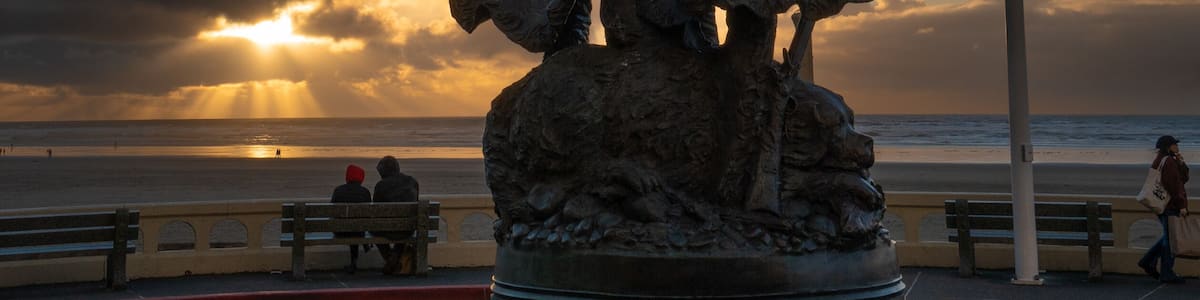 Eine Statue von zwei Figuren mit einer Flagge, einer Bank und einem Strand im Hintergrund.