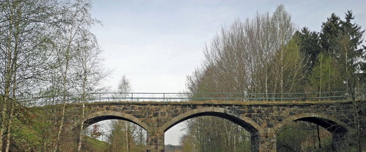 A stone railway bridge over tracks with a grassy area and trees on either side.
