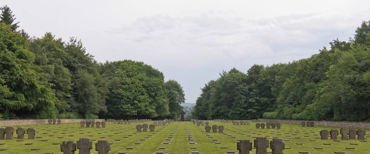 A cemetery with rows of headstones and crosses, surrounded by dense trees.