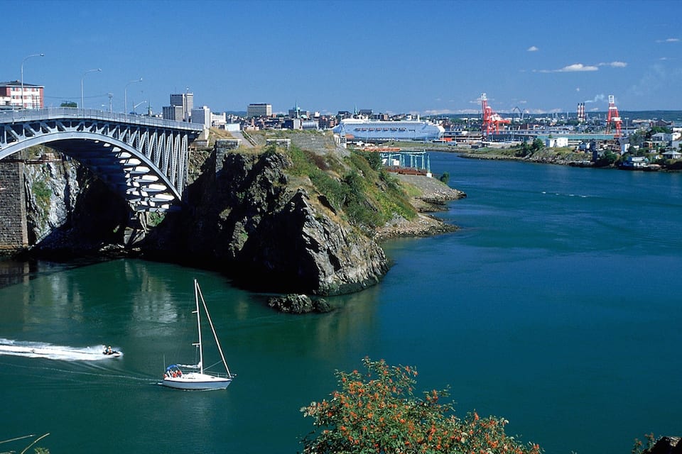 A bridge over a river, a sailboat, and a cityscape in the background.