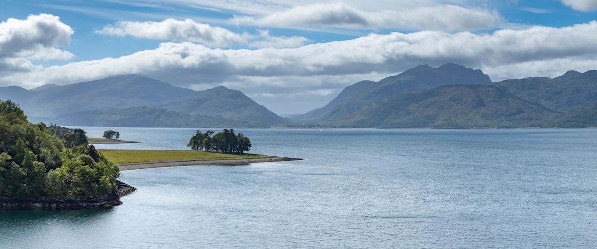 A calm lake surrounded by mountains and a small island with trees.