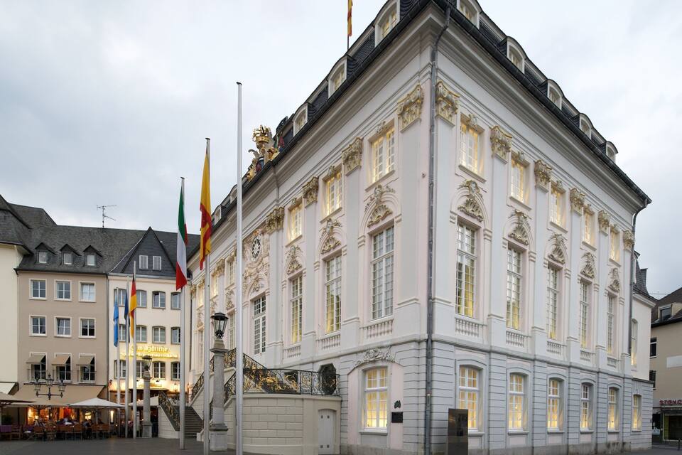 A historic building with ornate architecture, flags, and a café in the foreground.