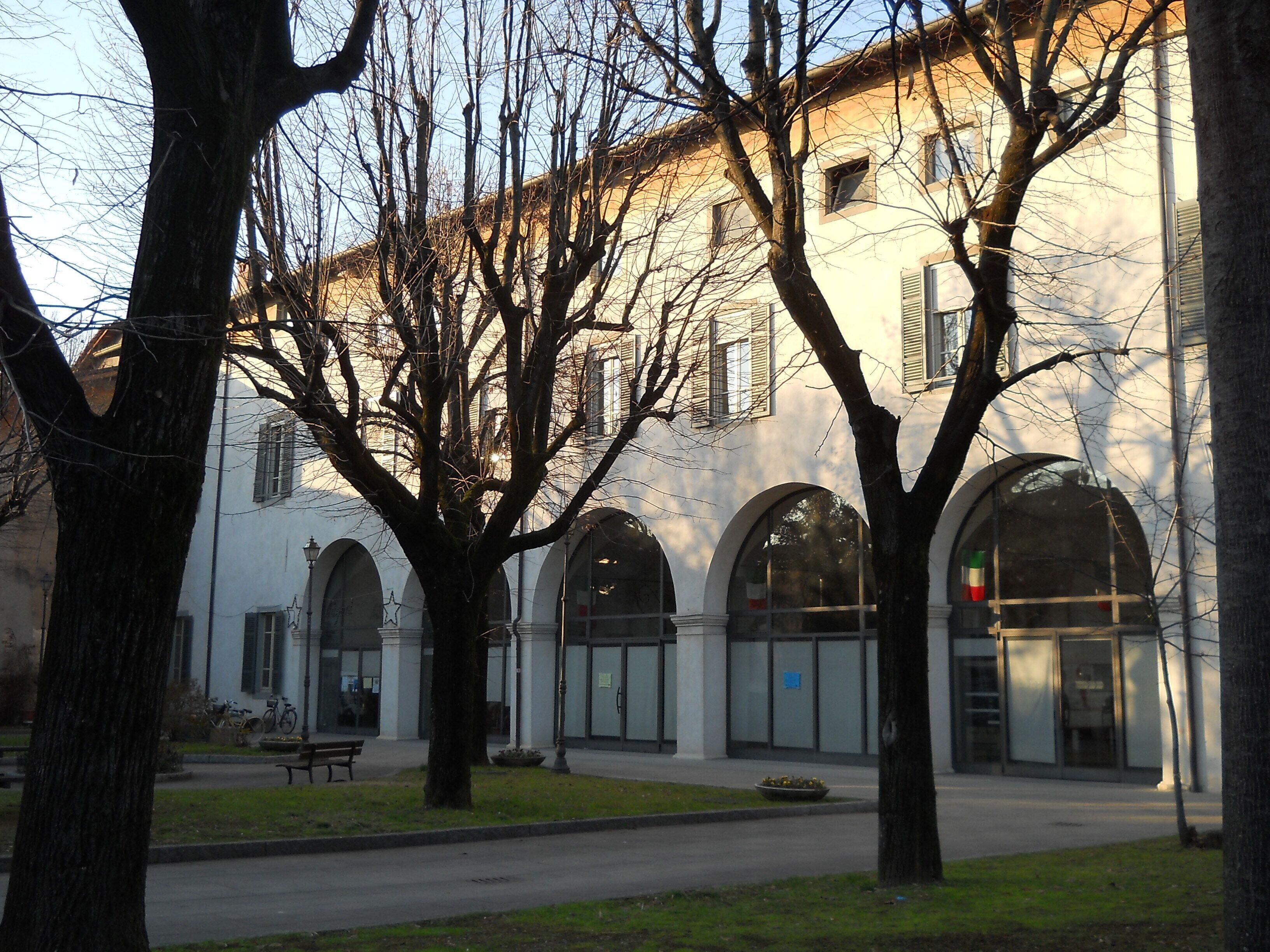 A building with arched windows and a courtyard with trees and a bench.