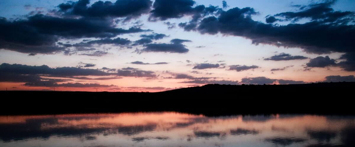 A sunset over a calm lake with silhouetted hills and scattered clouds.