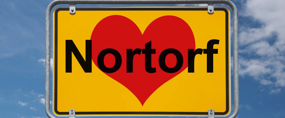 A sign with a heart and the word "Nortorf" against a blue sky with clouds.