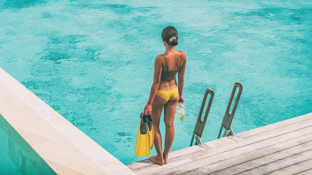 Luxury Bora Bora resort woman going snorkeling from overwater bungalow panoramic. Tahiti paradise destination vacation.