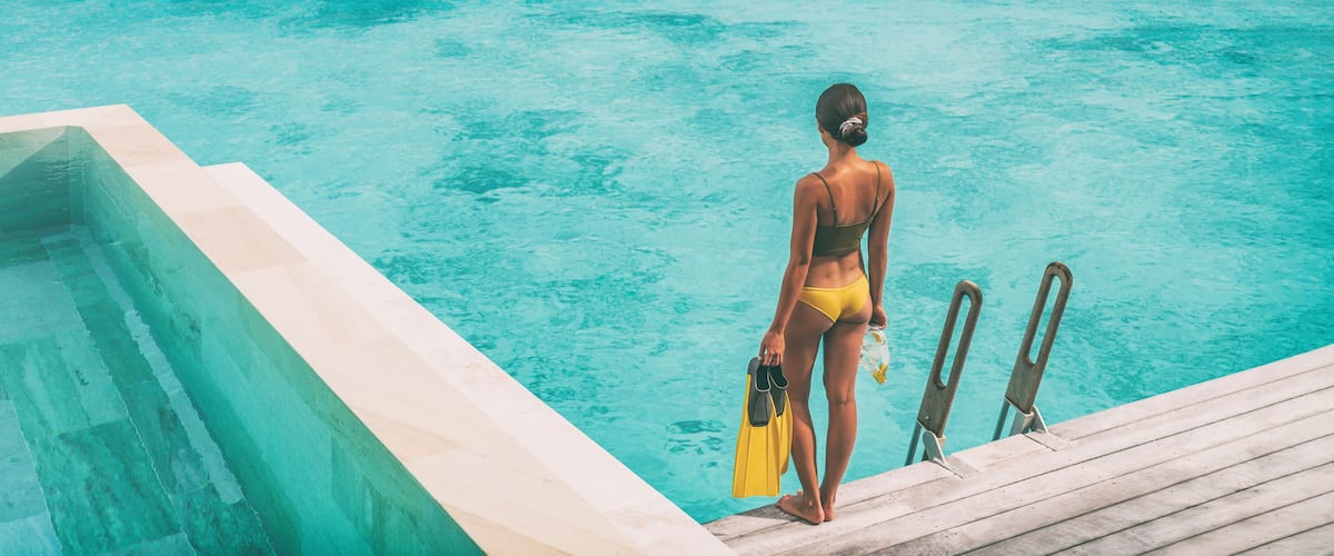 A woman in a yellow swimsuit standing at the edge of a swimming pool with diving boards.