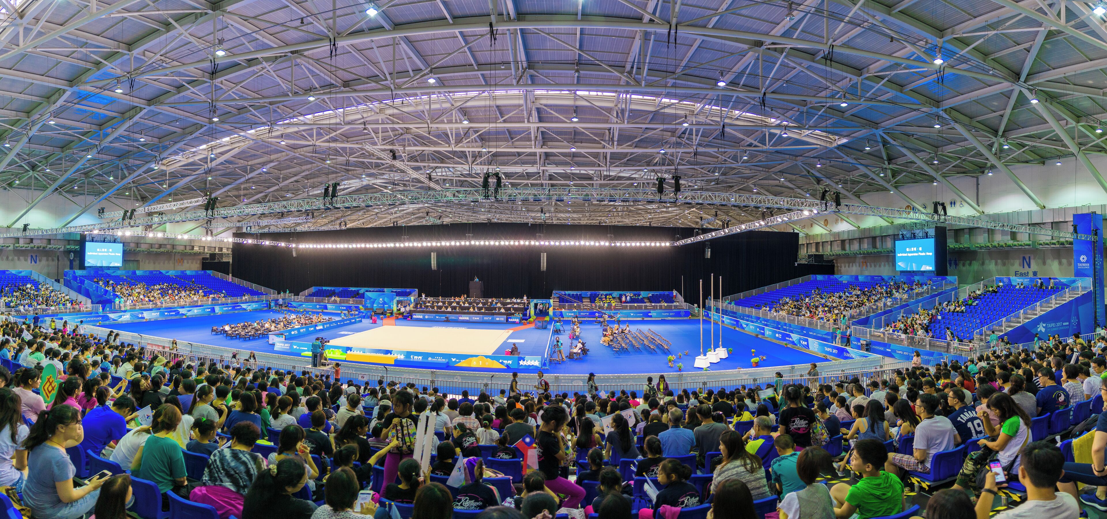 A large indoor stadium with a blue floor and a high ceiling.