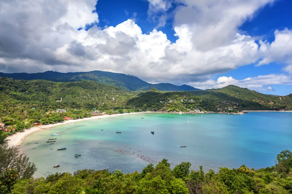 Un paisaje costero con una playa arenosa, aguas turquesas y colinas verdes.