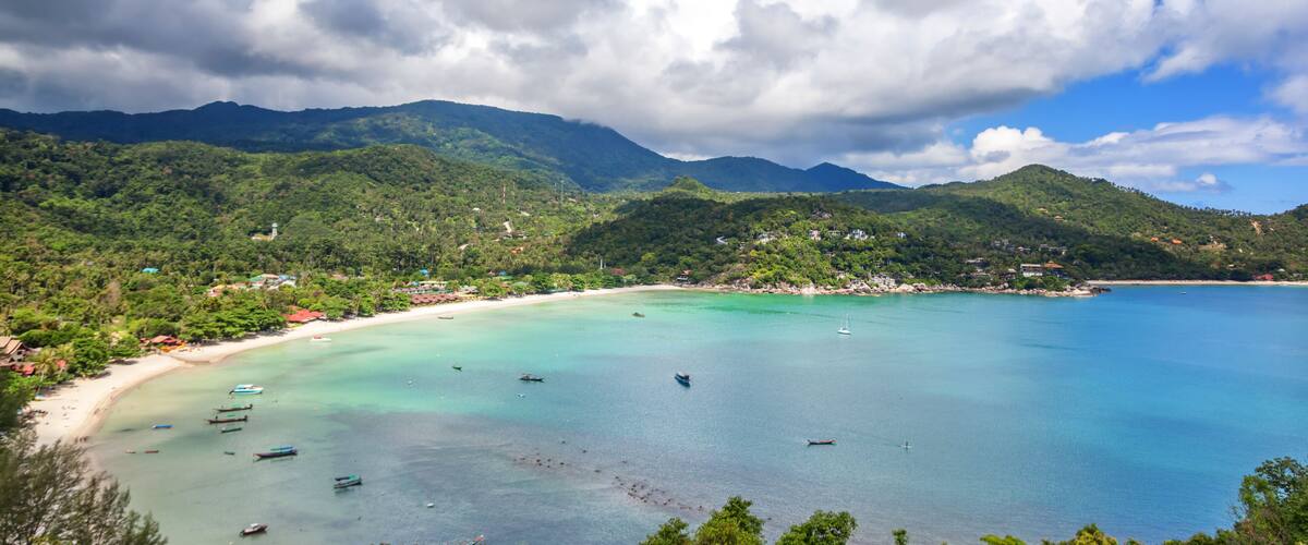A coastal landscape with a sandy beach, turquoise waters, and green hills.