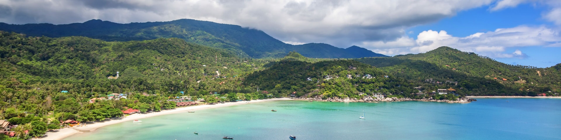A coastal landscape with a sandy beach, turquoise waters, and green hills.