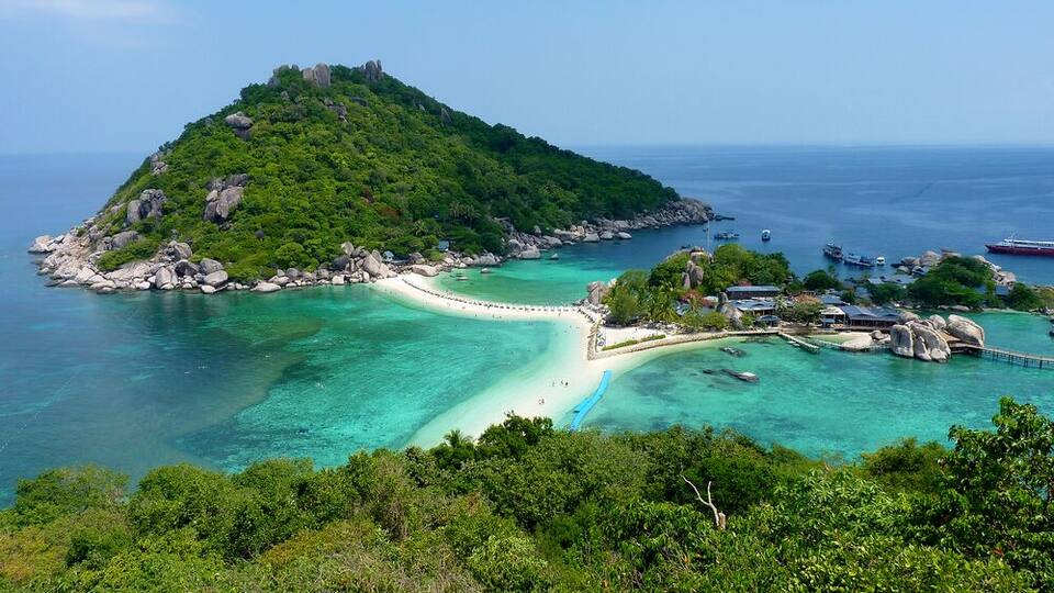 A tropical island with a white sandy beach, clear turquoise waters, and lush green vegetation.