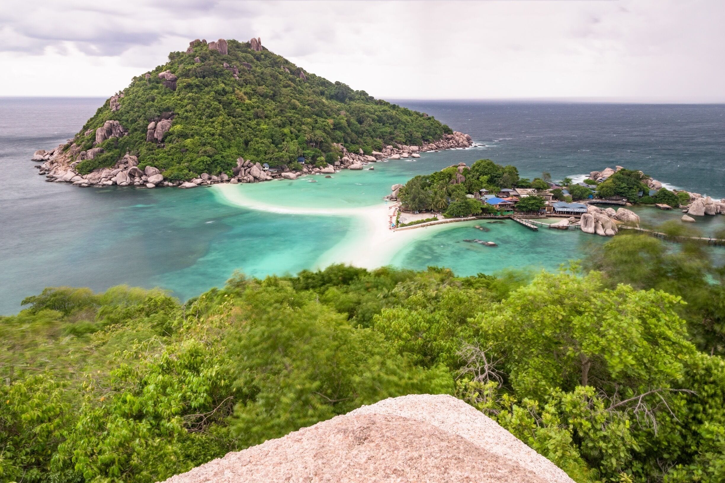 A tropical island with clear turquoise waters, lush greenery, and a small settlement with buildings and a dock.