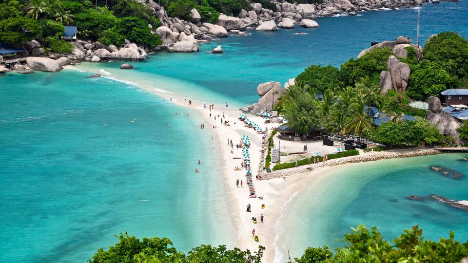 A tropical beach with clear turquoise waters, large rocks, and lush greenery.