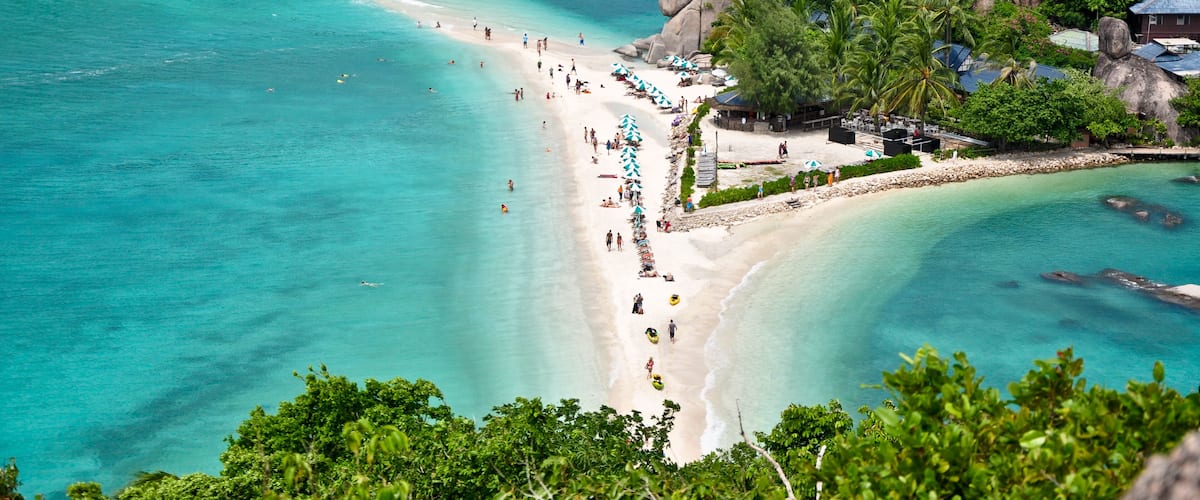 A tropical beach with clear turquoise waters, large rocks, and lush greenery.