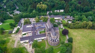 Vista aérea de um castelo histórico cercado por vegetação exuberante e edifícios modernos.