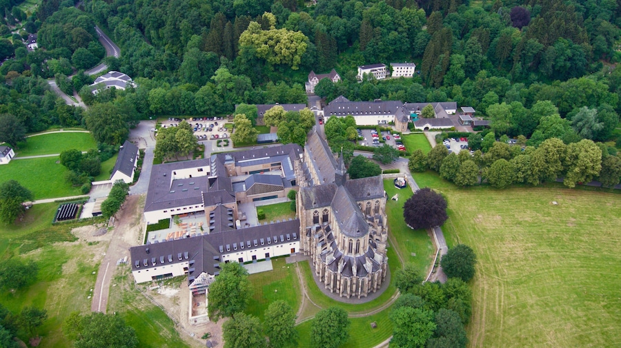 Eine Luftaufnahme einer historischen Burg, umgeben von üppiger Vegetation und modernen Gebäuden.