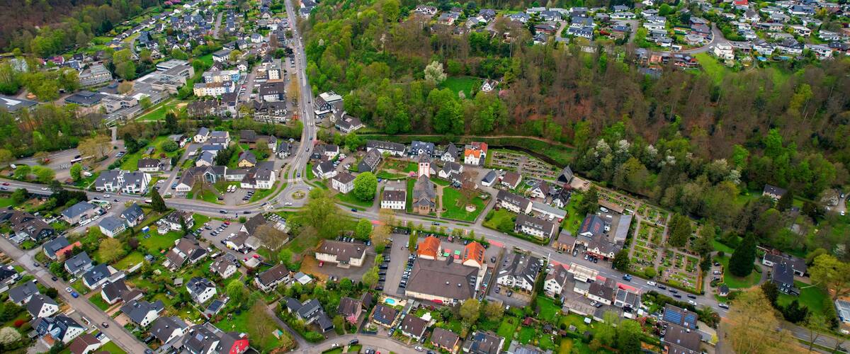 An aerial view of a residential area with houses, roads, and surrounding greenery.