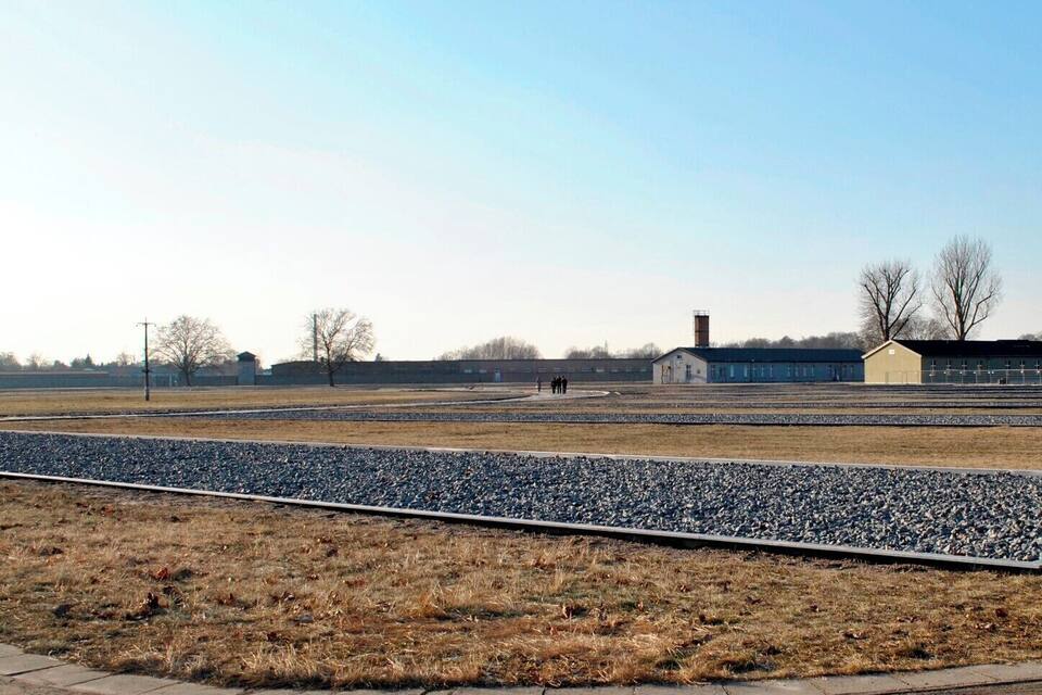A railway track with gravel beds, a grassy field, and a building in the background.