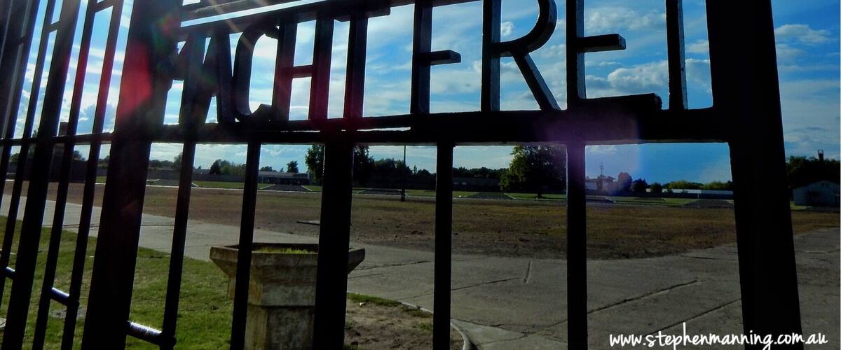 A metal gate with the words "ARBEIT MACHTE FREI" against a clear sky.