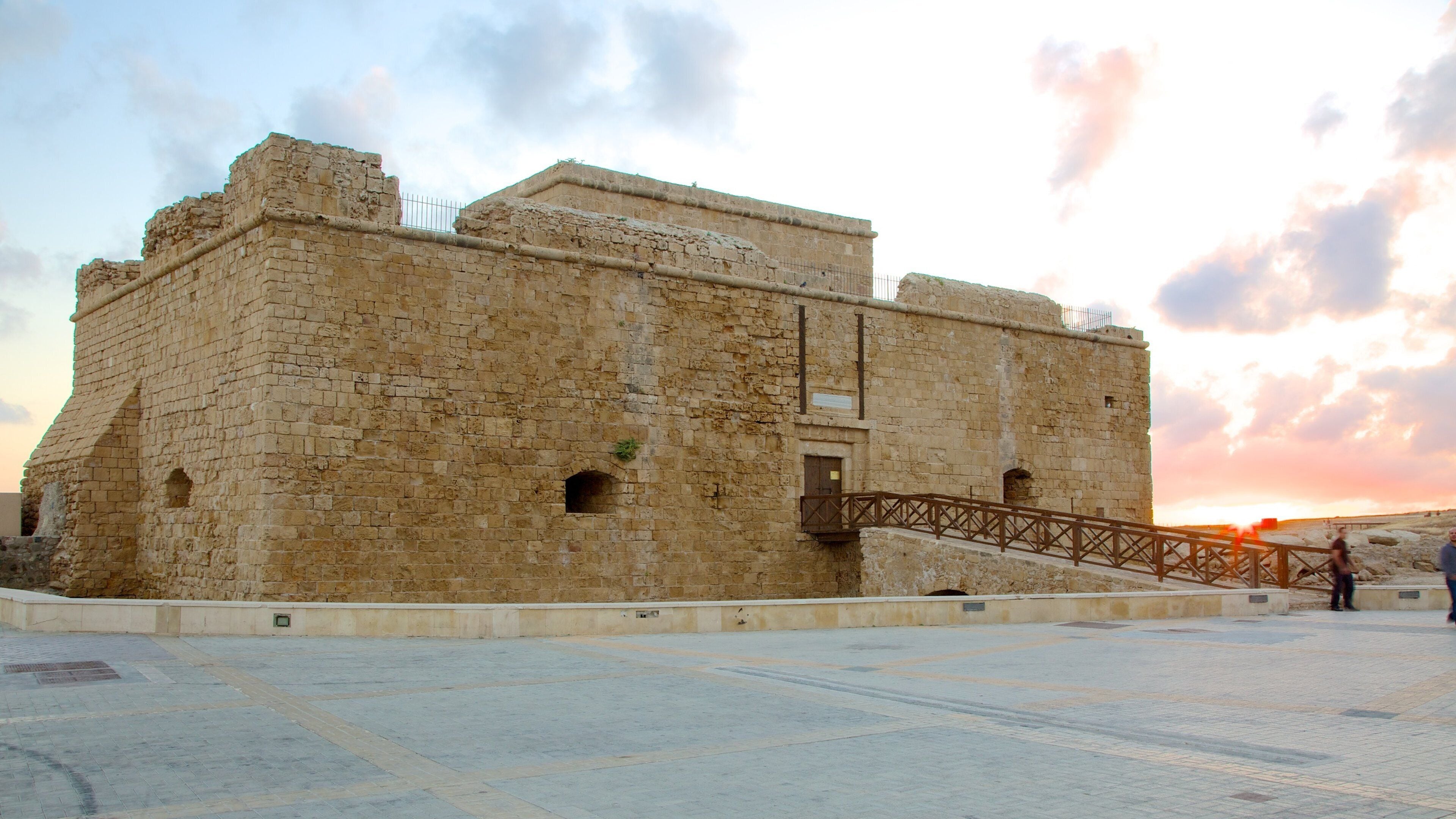 An ancient stone building with a wooden staircase leading up to a balcony.
