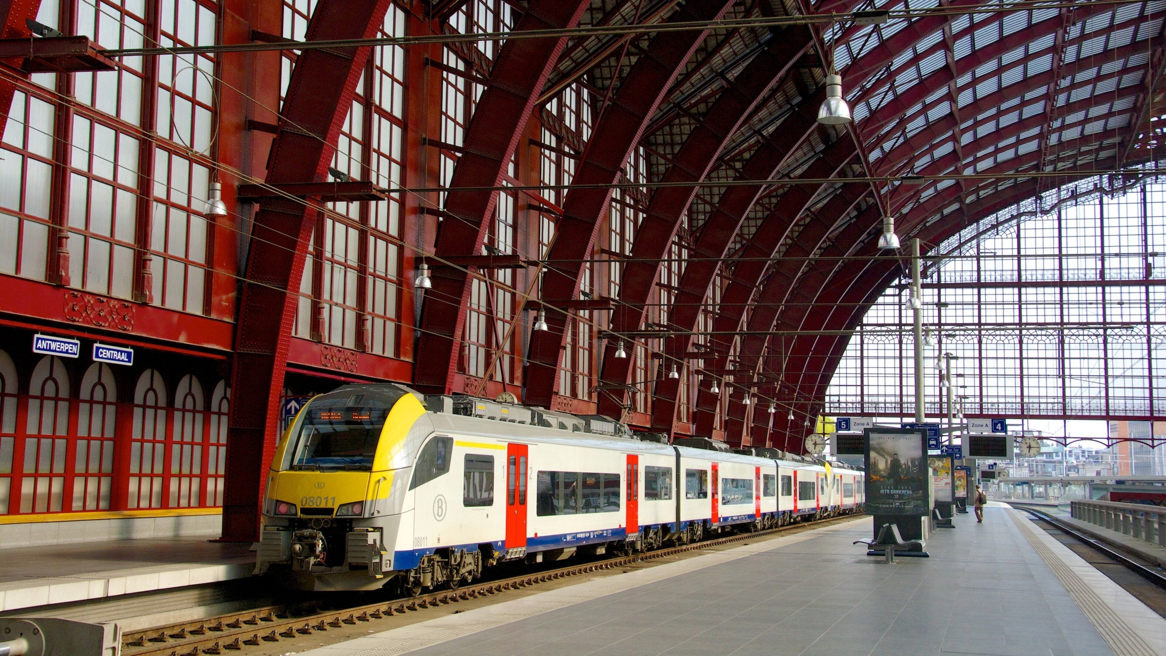 A modern train at a station with a red-brick facade and a large arched roof.