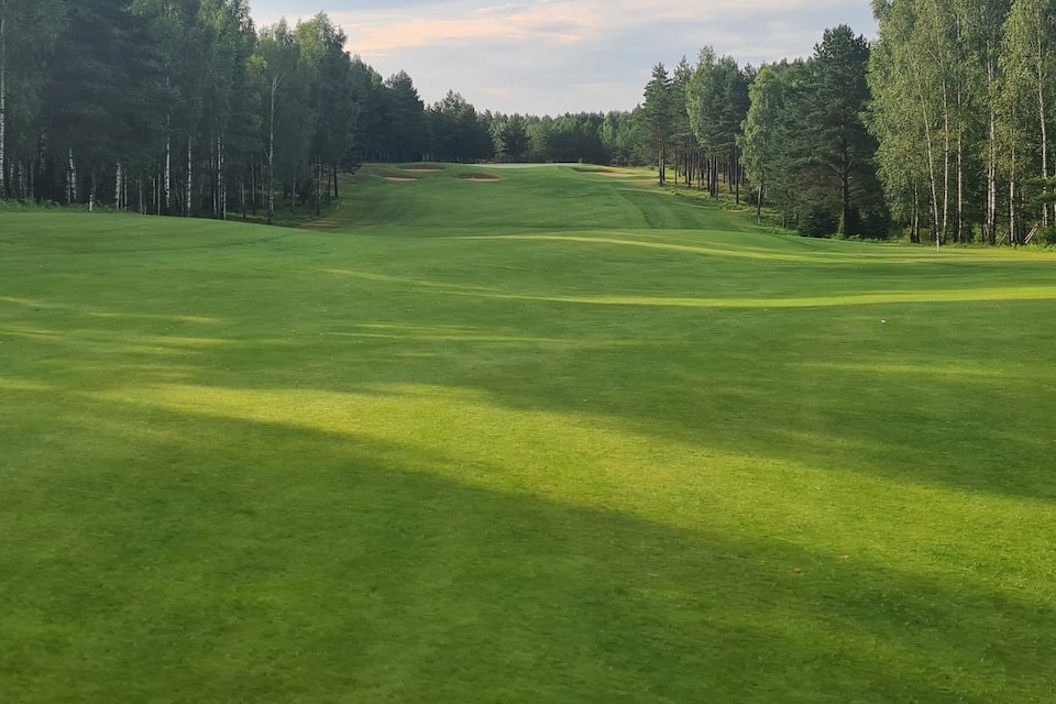 A golf course with a well-manicured green, sand bunkers, and a forested backdrop.